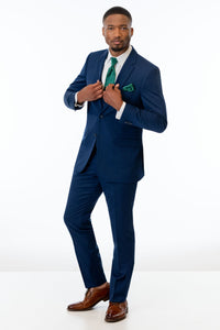 Man wearing Blue Performance Stretch Suit with a green tie and pocket square on a white background