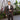 Man in a brown suit with white shirt and pink tie and pocket square standing outdoors on a patio