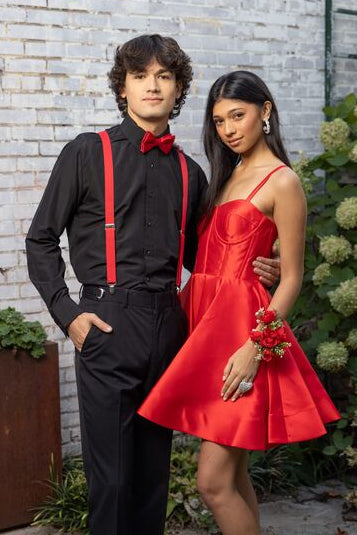 man in black pants, black shirt, red suspenders and bow tie posing with a woman in a red dress with a full skirt